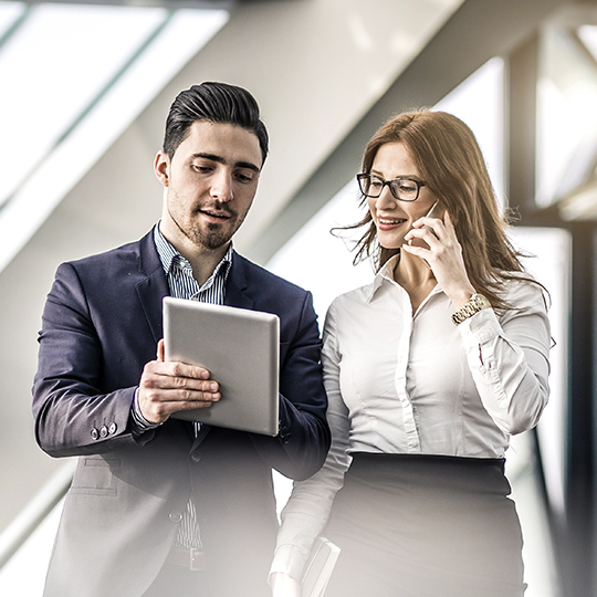 Man with a tablet showing device to a woman with a cellphone
