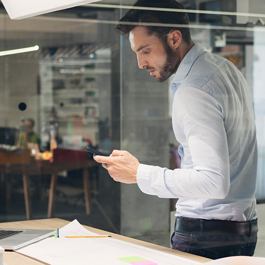man using a smartphone while standing over desk
