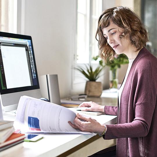 Woman looking at paperwork in front of computer.